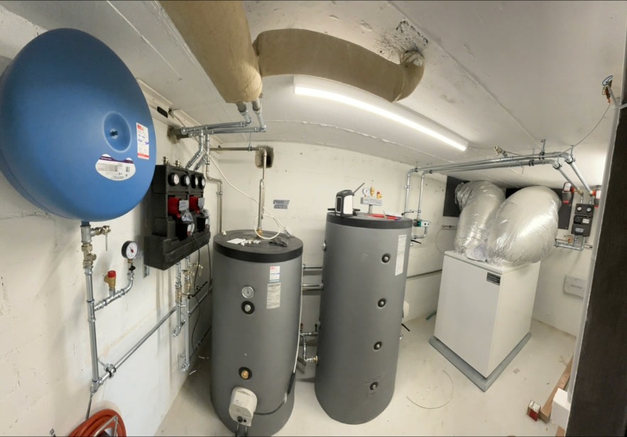 Heizraum Panorama – Wärmepumpe & Lüftung – Panoramaansicht des Technikraums mit Speichern, Pumpengruppe, Ausdehnungsgefäss und Lüftungsgerät mit isolierten Kanälen.